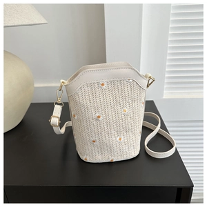 Detailed view of woven daisy patterns on straw bucket bag with elegant faux leather trim