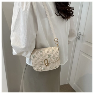 Detail of woven straw crossbody bag with floral embroidery and golden metal lock