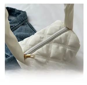 Close-up of white quilted cylinder bag featuring precise stitching and gold metal zipper