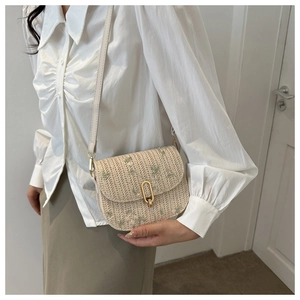 Detail of woven beige crossbody bag with floral embroidery and gold U-shaped buckle