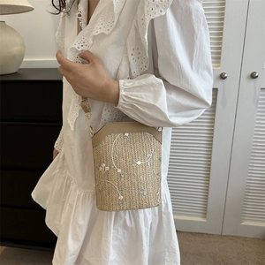 Straw bucket crossbody bag with white flower embroidery and gold chain strap worn by model