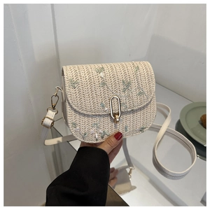 Close-up of woven straw crossbody bag featuring green leaf embroidery and gold metal clasp