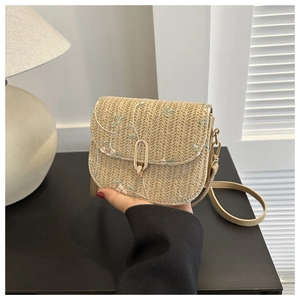 Detailed view of floral embroidery and gold metal clasp on beige woven shoulder bag