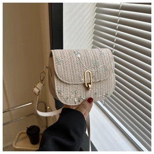 Detail of straw woven saddle bag featuring floral embroidery and gold U-shaped metal clasp
