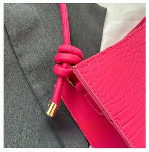 Détail du sac à main rose fuchsia texture crocodile avec nœud et finitions métalliques dorées