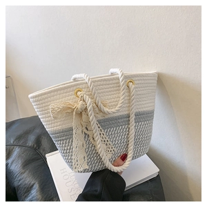 Détail du sac seau tressé bicolore avec surpiqûres et décoration de nœud en dentelle