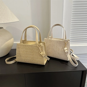 Minimalist straw woven crossbody bag in khaki and beige on a sleek wooden surface