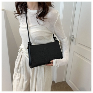 Détail du sac sous le bras en cuir noir texture crocodile avec bandoulière à nœud