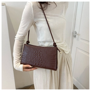 Détail d'un sac bandoulière marron à motif crocodile avec un nœud sur la lanière