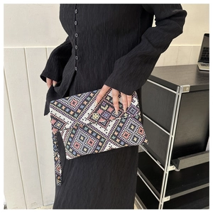 Close-up of the woven fabric texture and golden clover metal clasp on the ethnic clutch