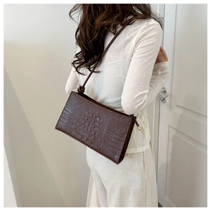 Détail d'un sac à bandoulière rectangulaire marron foncé motif crocodile porté