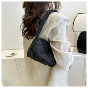 Close-up of a black quilted shoulder bag with diamond stitching on a model's arm