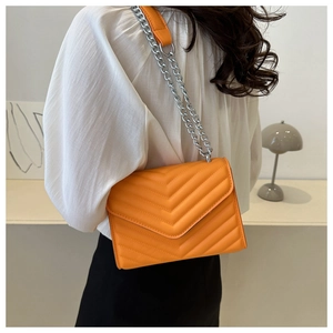 Detail of bright orange crossbody bag with V-shaped quilting and silver chain strap