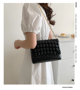 Detail of black pleated crossbody bag with premium gold chain strap on white dress