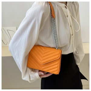 Close-up of bright orange chevron quilted shoulder bag with silver chain strap on model