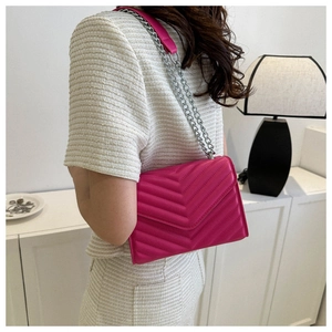 Detail of the vibrant fuchsia crossbody bag with V-quilted pattern and silver chain strap