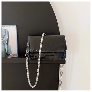 Detail shot of black patent leather crossbody bag with crocodile texture and silver chain