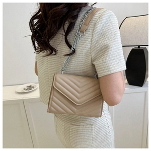 Detail of beige quilted crossbody bag with silver chain strap worn by a model