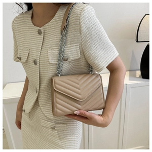 Quilted beige shoulder bag with silver chain strap shown worn by a model in a minimal setting