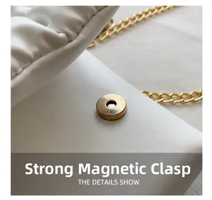 Detail of a strong magnetic gold clasp on a white pleated crossbody bag with metal chain