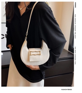 Détail du sac bandoulière blanc en croissant avec boucle dorée sur un pull noir