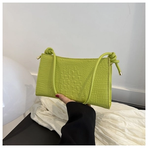 Détail d'un sac à bandoulière vert effet crocodile avec lanières nouées et embouts dorés
