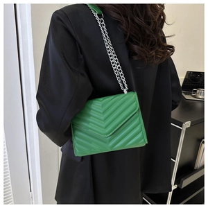Close-up of green quilted leather bag with silver chain strap worn with black blazer