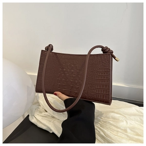 Détail du sac sous le bras marron texture crocodile avec nœud décoratif sur bandoulière