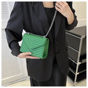 Detail of green chevron quilted crossbody bag with silver chain strap on model