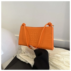 Détail d'un sac sous le bras en similicuir orange crocodile avec bandoulière à nœuds
