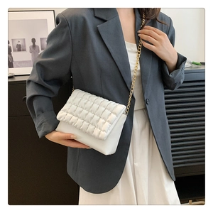 Close-up of a white quilted bubble bag with gold chain strap worn on a grey blazer