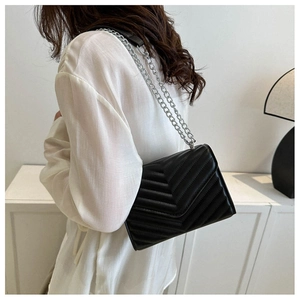 Detail of minimalist black crossbody bag with V-shaped quilting and silver chain strap