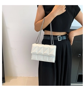 Detail of white quilted crossbody bag with silver chain strap worn by a model