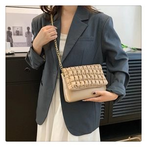 Detail of a beige pleated bubble crossbody bag with golden chain strap on a model