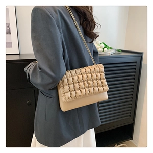 Beige quilted pleat handbag with gold chain strap shown on model for shoulder wear