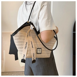 Detail of woven straw tote bag featuring black leather trim and chic lettered ribbons