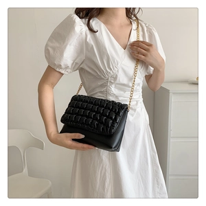 Detail of black pleated texture shoulder bag with gold chain strap on white dress