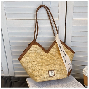 Detail of straw woven tote bag featuring a V-shaped top, leather trim, and fashion patch