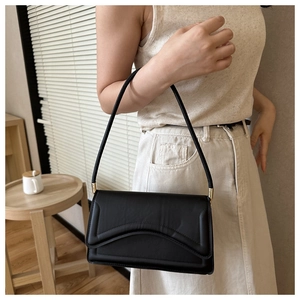 Detail of black faux leather underarm bag featuring wave curve flap and gold hardware