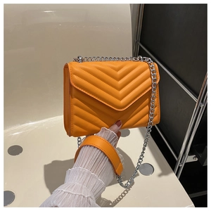 Detailed close-up of orange crossbody bag with V-shaped chevron quilting and silver chain