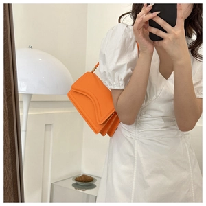 Detail view of bright orange pleated accordion shoulder bag with structured V-shape flap