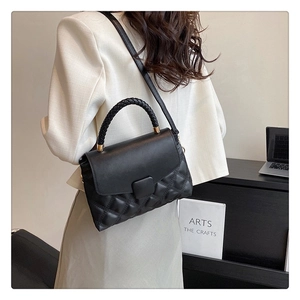Détail du sac bandoulière matelassé noir avec poignée tressée et accents dorés sur modèle