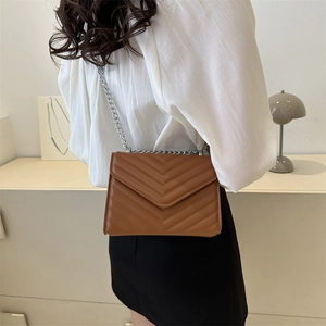 Brown quilted crossbody bag with silver chain strap shown on a minimalist stand