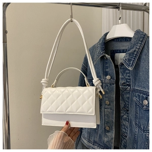 Detailansicht einer weißen Stepptasche mit goldenem Drehverschluss und Knoten am Schultergurt