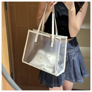 Detail of transparent PVC tote bag with colorful rhinestones and cream leather handles