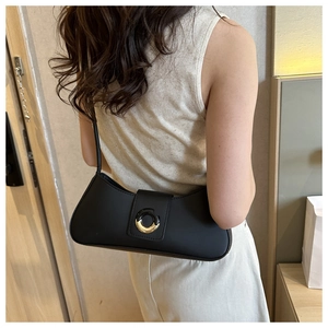 Close-up of minimalist black baguette bag with gold metal buckle on a shoulder strap