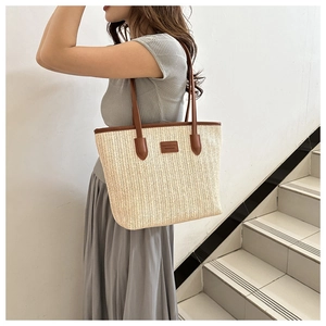 Detail of cream straw tote bag with brown leather handles and fashion logo patch