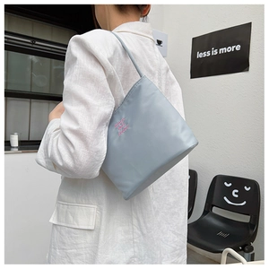 Close-up of stylish nylon shoulder bag with pink embroidery on a gray-blue surface
