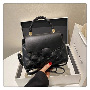 Détail du sac à bandoulière matelassé noir avec poignée tressée sur fond de boîte cadeau