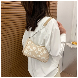Detailed view of floral embroidery and metallic chain on a beige shoulder bag